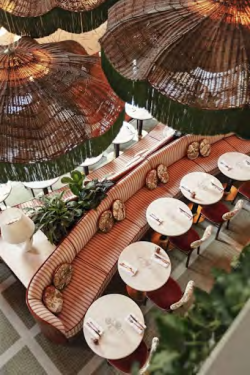 A chic cafe with curved red booths, white round tables, red chairs, and hanging wicker umbrellas creating a cozy outdoor dining vibe.