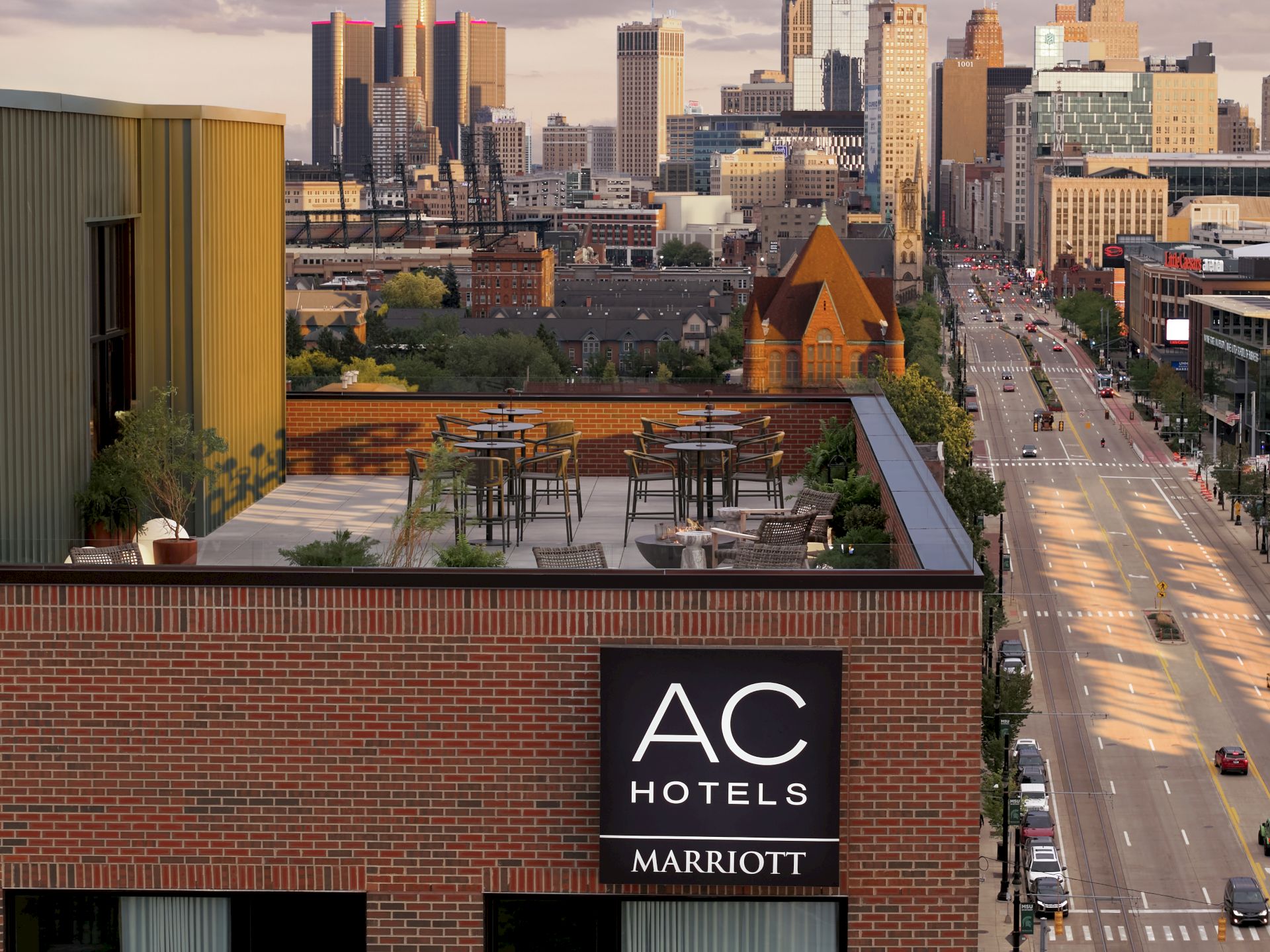 Downtown skyline at dusk with busy traffic below and an AC Hotels by Marriott rooftop terrace sign in the foreground.