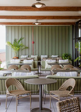 An elegant patio lounge with rattan chairs and sofas, round tables, green drapes, and two ceiling pendant lights.