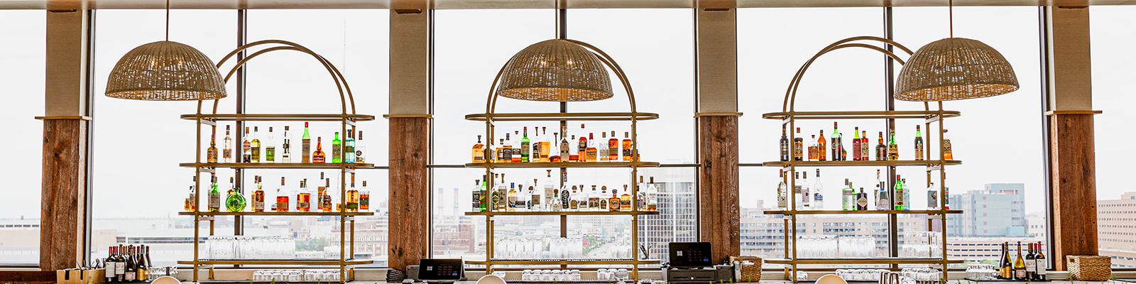 A stylish rooftop bar with backlit shelves of colorful bottles and hanging wicker lamps overlooking the city.