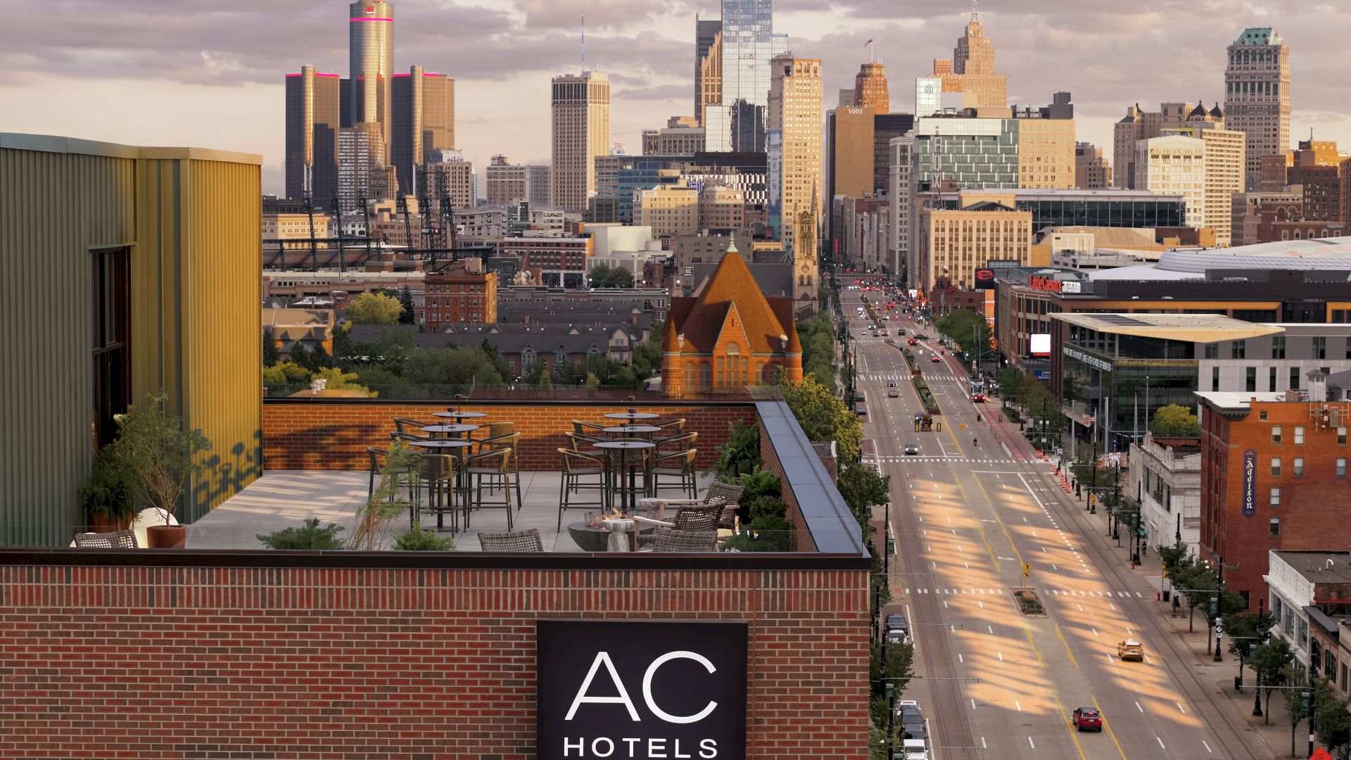 A city skyline at dusk viewed from a hotel rooftop terrace, with an AC Hotels Marriott sign in the foreground.