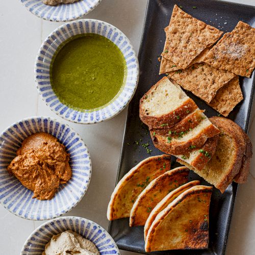 Plates of sliced pita/bread with hummus-like dips and a green herb/olive-oil sauce.