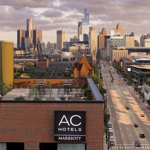 A downtown city skyline at dusk with skyscrapers, a busy avenue, and an AC Hotels Marriott sign in the foreground.